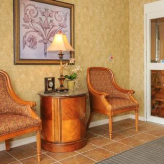 A cozy interior featuring two upholstered chairs flanking a wooden table with a lamp, set against a patterned wallpaper backdrop.
