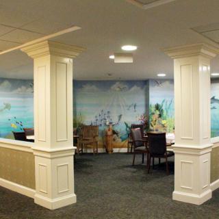 A cozy dining area featuring elegant columns, comfortable seating, and a scenic mural on the wall.
