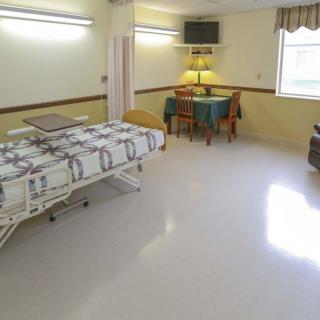 A hospital room with a bed, table, chairs, and a lamp.