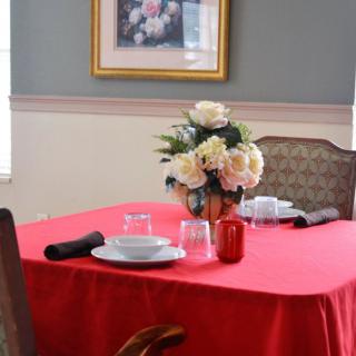 A dining table set with a red tablecloth, adorned with a bouquet of flowers, plates, glasses, and napkins.