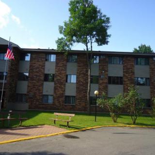 A brick apartment building with a flagpole and a well-maintained lawn.