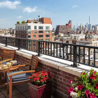 A rooftop terrace with a view of the city skyline, featuring outdoor seating and vibrant plants.