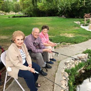 Three elderly people enjoying a peaceful day fishing by the pond.