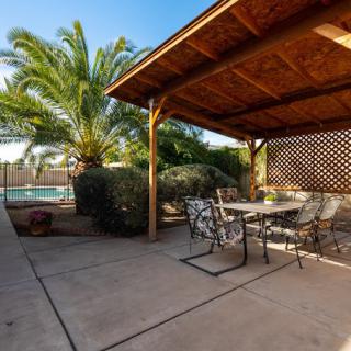A sunny backyard patio with a pergola and outdoor furniture, surrounded by palm trees.