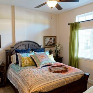A cozy bedroom with a large bed, colorful pillows, and a ceiling fan.