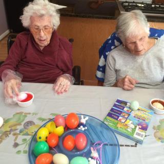 Two elderly women painting colorful Easter eggs together at a table.