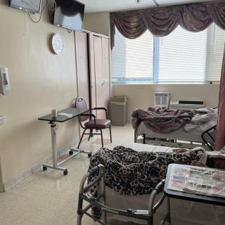 A hospital room with a patient bed, medical equipment, and a chair next to a window with curtains.