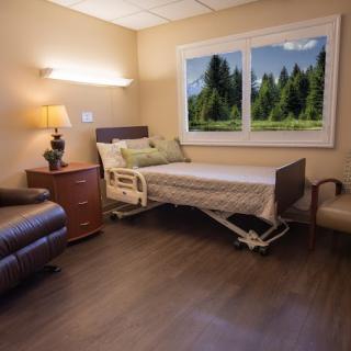 A well-furnished hospital room with a bed, chair, and a scenic view from the window.