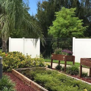A peaceful garden area with benches, surrounded by lush vegetation and a white fence.