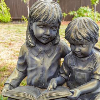 A statue of two children reading a book together in an outdoor setting.