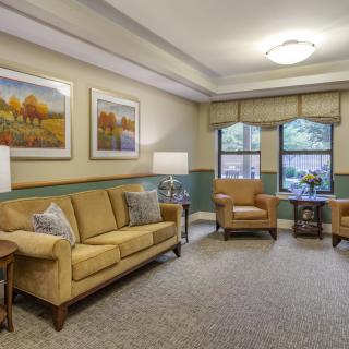 A cozy and well-decorated living room featuring a sofa and armchairs, with paintings adorning the walls.