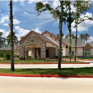 A large, modern house with stone exterior and a well-maintained driveway surrounded by trees under a clear sky.