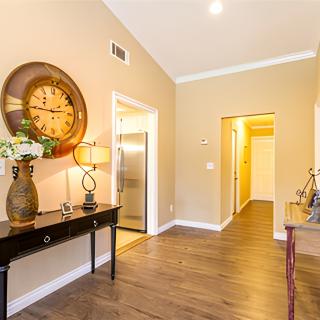 A warmly lit hallway featuring a large wall clock, elegant furniture, and wooden flooring.