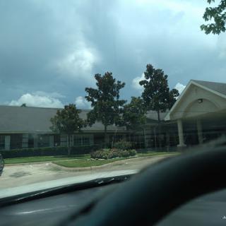 A view of a residential building under a cloudy sky, taken from inside a vehicle.