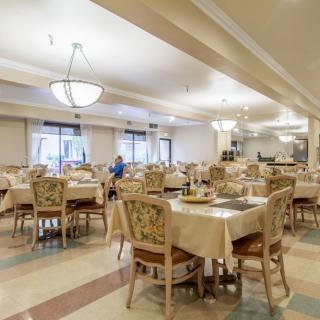 An elegant and spacious dining room with neatly arranged tables and chairs, illuminated by chandeliers.