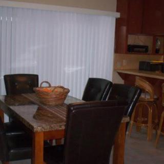 A dining area featuring a table with chairs and a basket centerpiece, adjacent to a kitchen.