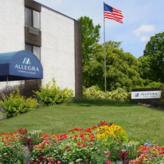A building with an awning and a U.S. flag, surrounded by colorful flowers and greenery.