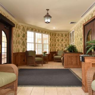 A cozy waiting room with armchairs and a front desk, featuring patterned wallpaper and large windows.