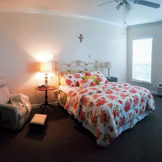 A cozy bedroom with floral bedding, a bedside lamp, and a comfortable chair by the window.