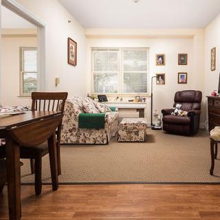 A cozy living room with a dining table, floral sofas, and an armchair by the window.