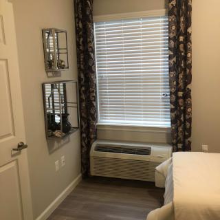 A cozy bedroom with a window adorned with patterned curtains and blinds, featuring a bed and decorative mirrors on the wall.