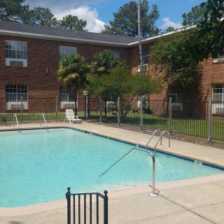 A small outdoor swimming pool surrounded by a fence, with a brick building in the background on a sunny day.
