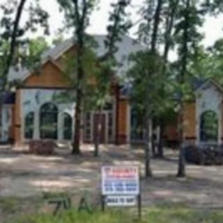 A suburban house surrounded by trees with a 'For Sale' sign in front.