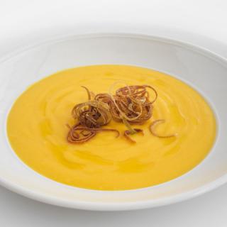 A bowl of creamy pumpkin soup garnished with crispy onion straws.