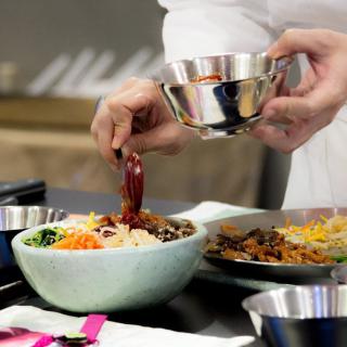 A person preparing bibimbap by adding spicy sauce to a bowl of vegetables and rice.