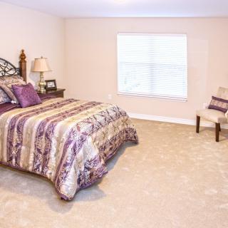 A cozy bedroom with a patterned bedspread, carpet flooring, and a window.