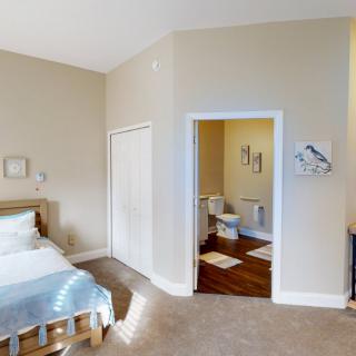 A cozy bedroom with a view into an adjoining bathroom, featuring neutral tones and simple decor.
