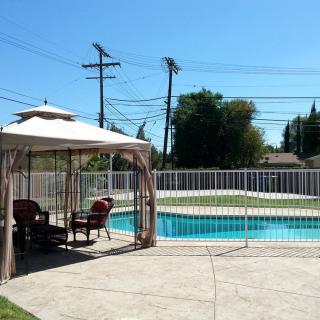 A sunny backyard with a swimming pool, gazebo, and outdoor seating area.