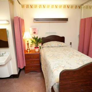 A well-furnished hospital room featuring a bed, nightstand, lamp, and privacy curtains.