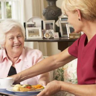 A caregiver assists an elderly woman with a meal in a home setting.