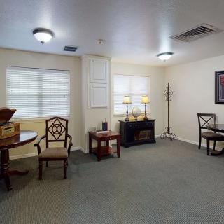 A cozy room interior with chairs, a table, lamps, and windows.