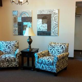 A cozy living room setup featuring patterned armchairs, a side table with a lamp, and abstract art on the wall.