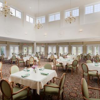 A spacious and elegantly decorated dining room with neatly arranged tables and chairs, illuminated by chandeliers.