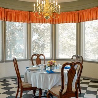 Elegant dining room with a round table set for breakfast, featuring large windows and a classic chandelier.