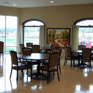 A dining area with several tables and chairs, large windows, and a painting on the wall.