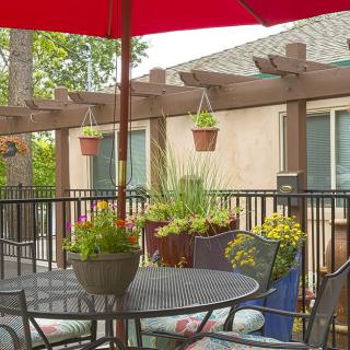 A cozy patio with outdoor seating under a red umbrella, surrounded by potted and hanging plants.