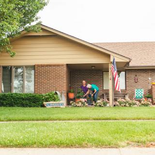 Two people tending to the garden in front of a charming house.