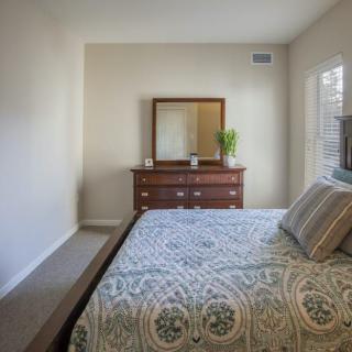 A cozy bedroom with a neatly made bed, a wooden dresser with a mirror, and plenty of natural light.