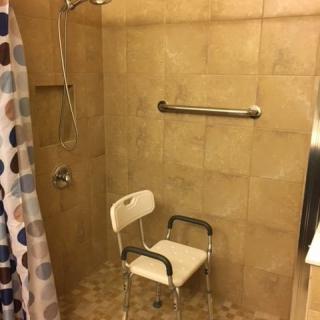 A bathroom with a tiled shower area featuring a shower chair and a grab bar for accessibility.