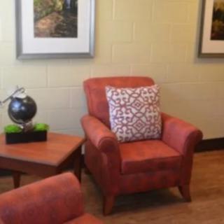 A cozy living room featuring an orange armchair with a patterned pillow, surrounded by framed artwork and a globe on a side table.