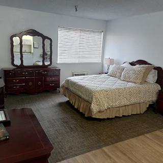 A cozy and well-furnished bedroom featuring a bed, dresser with a mirror, and a soft carpet.
