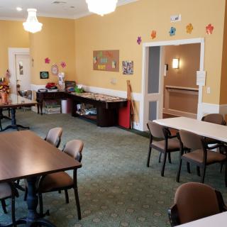 A well-lit community room with tables, chairs, and art supplies arranged for activities.