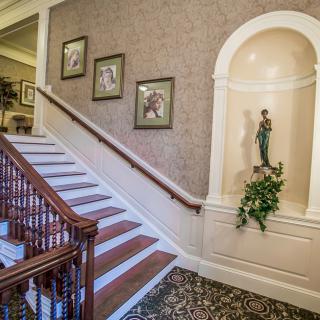 A classic interior with a staircase adorned by framed artwork and a statue in a niche.
