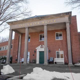 A brick building with tall columns and an entrance, surrounded by snow in a winter setting.