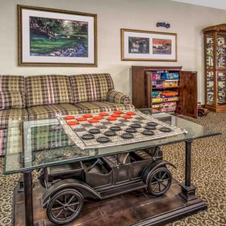 A cozy living room with a plaid couch, a glass coffee table featuring a checkers board game, and colorful artwork on the walls.