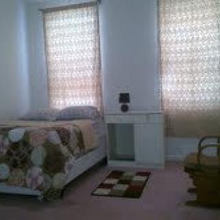 A simple bedroom with a bed, small desk, and two windows with curtains.